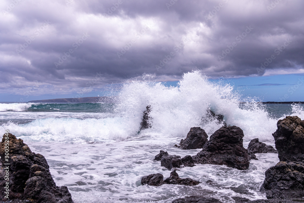 Huge wave splashes on a rocky beach. A large lava rock completely covered in a white ocean spray, La Perouse bay, Maui,, Hawaii