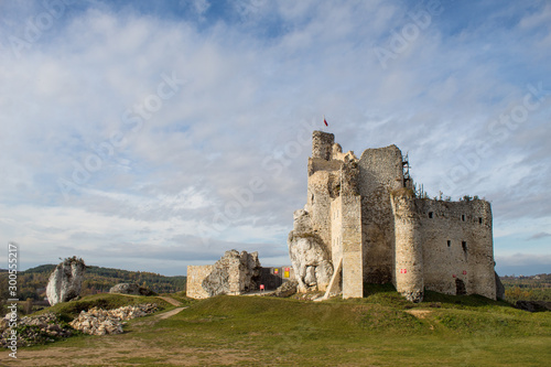 The ruins of a medieval European castle against the backdrop of a rocky ridge, blue sky, coniferous forest and green meadows. photo