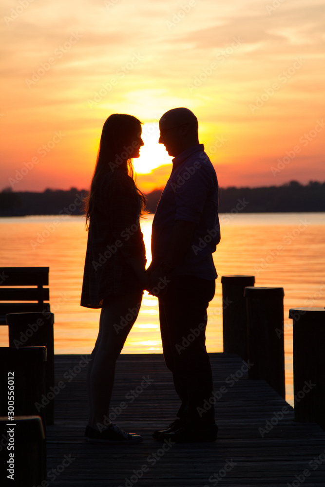 The silhouette of a male and female straight heterosexual couple getting romantically closer together on a dock at sunset The silhouette of a male and female straight heterosexual couple getting romantically closer together on a dock at sunset