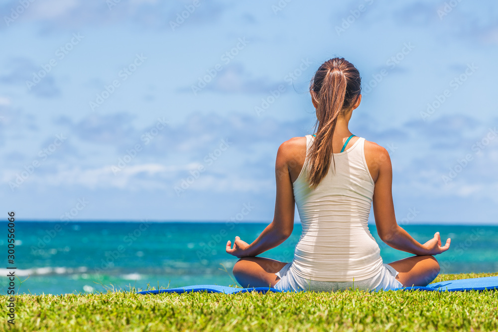 Yoga meditation woman meditating in lotus pose on exercise mat on beach grass.