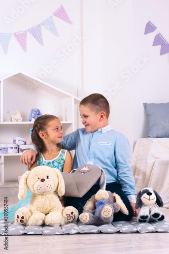 beautiful boy and girl sitting on the floor in the children's room among the toys, the boy hugs the girl and they look at each other