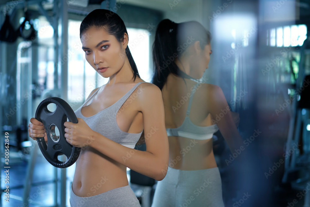 Fototapeta premium Asian sporty doing exercise with disassembled barbell or dumbbell at fitness gym. Woman taking weight loss for slim. Healthy sport cardio strong. Fitness muscular body.