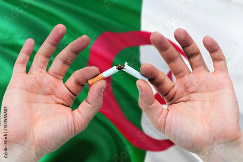 Algeria quit smoking cigarettes concept. Adult man hands breaking cigarette. National health theme and country flag background.