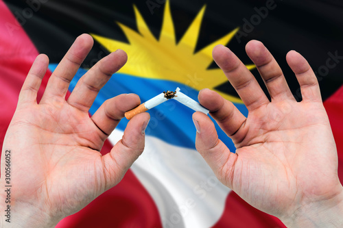 Antigua and Barbuda quit smoking cigarettes concept. Adult man hands breaking cigarette. National health theme and country flag background.