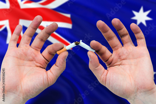 Australia quit smoking cigarettes concept. Adult man hands breaking cigarette. National health theme and country flag background.