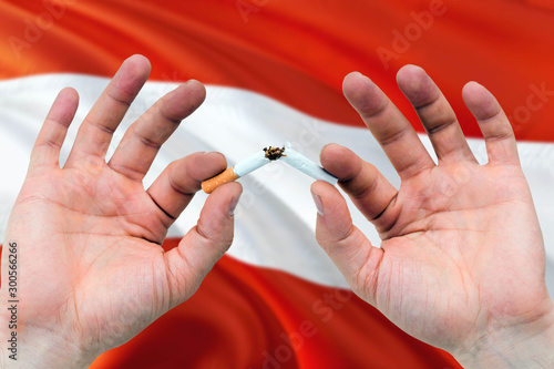 Austria quit smoking cigarettes concept. Adult man hands breaking cigarette. National health theme and country flag background.