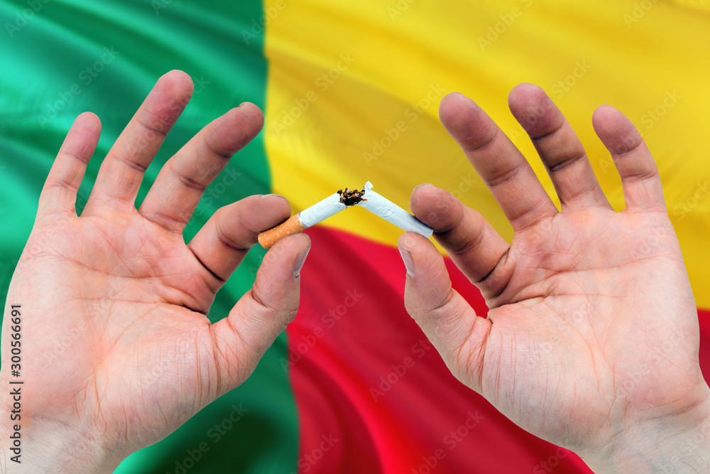Benin quit smoking cigarettes concept. Adult man hands breaking cigarette. National health theme and country flag background. Benin quit smoking cigarettes concept. Adult man hands breaking cigarette. National health theme and country flag background.