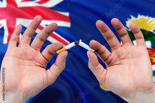 Cayman Islands quit smoking cigarettes concept. Adult man hands breaking cigarette. National health theme and country flag background.
