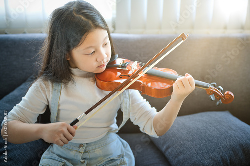 Photo Asian kid learning and practising  to play violin at home