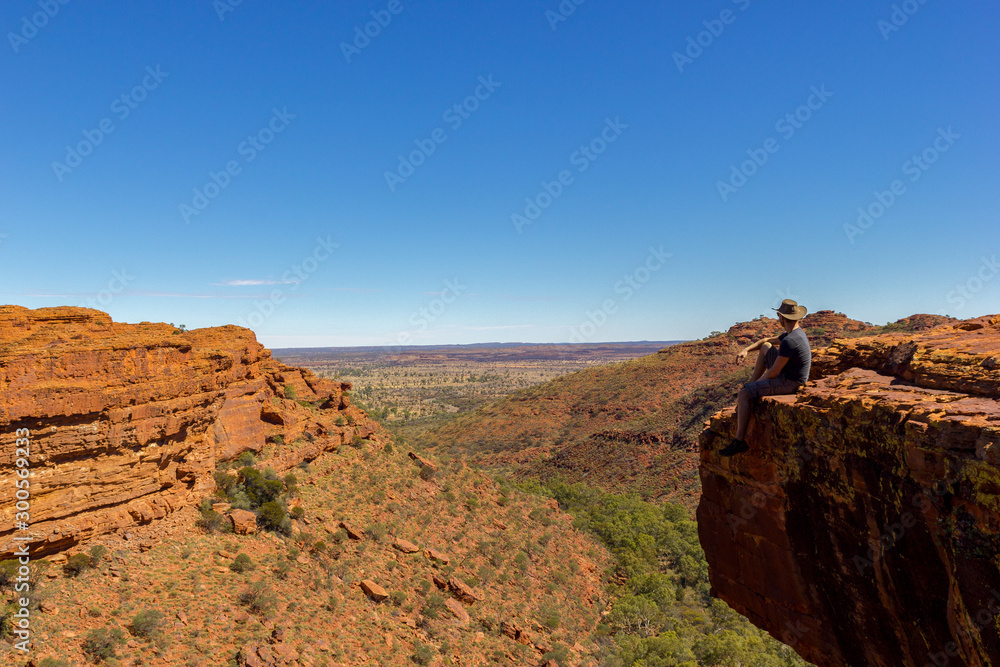 Fototapeta premium young man enyoing view of a Canyon and sitting on the edge of a cliff, Watarrka National Park, Northern Territory, Australia