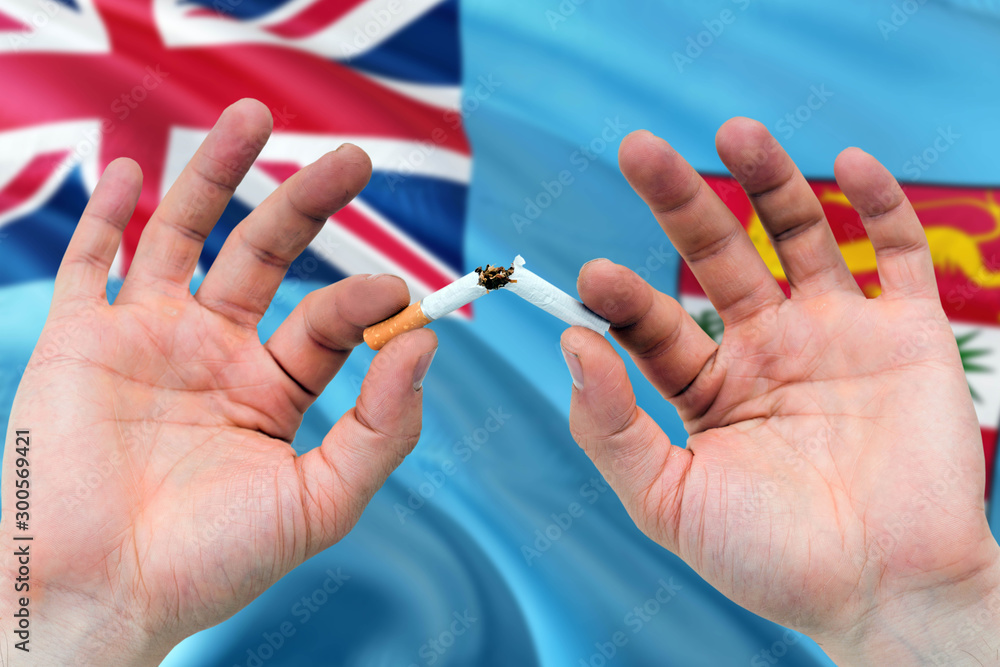 Fiji quit smoking cigarettes concept. Adult man hands breaking cigarette. National health theme and country flag background.