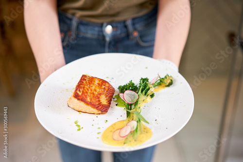 The waiter holds in his hands Salmon steak fillet and garnished with young broccoli. Restaurant menu, a series of photos of different dishes