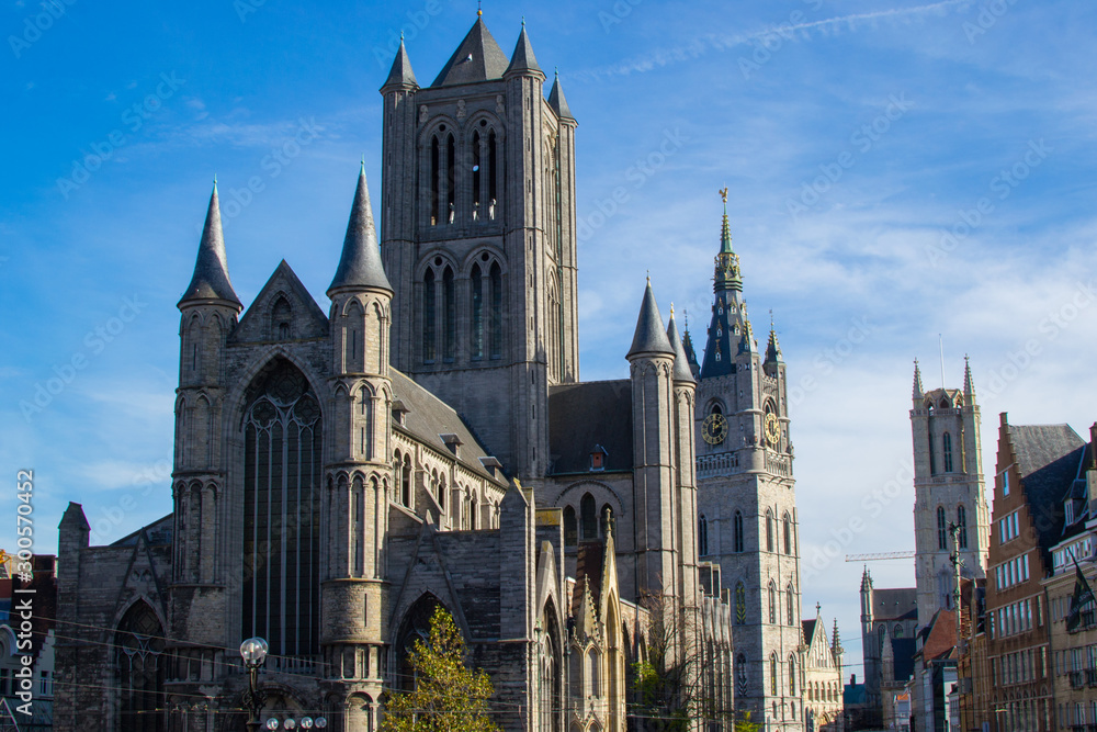 Facade of Saint Nicholas' Church (Sint-Niklaaskerk) with the clock tower of Belfry of Ghent (Het Belfort) and Saint Bavo Cathedral (Sint-Baafskathedraal) at the background, in Ghent, Belgium