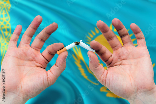Kazakhstan quit smoking cigarettes concept. Adult man hands breaking cigarette. National health theme and country flag background.