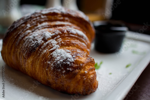 croissant in powdered sugar on a white plate. apricot jam in a black little plate next to a croissant