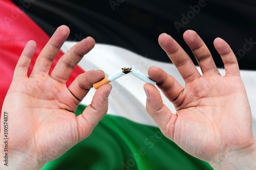 Palestine quit smoking cigarettes concept. Adult man hands breaking cigarette. National health theme and country flag background.