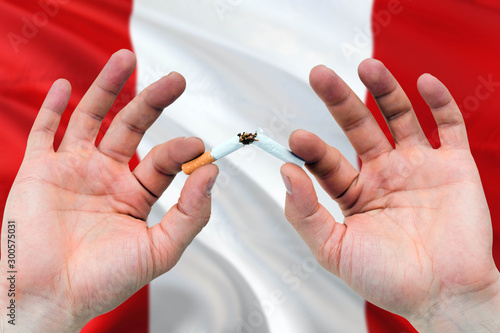 Peru quit smoking cigarettes concept. Adult man hands breaking cigarette. National health theme and country flag background.