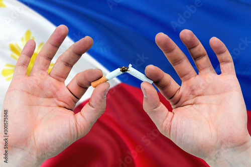 Philippines quit smoking cigarettes concept. Adult man hands breaking cigarette. National health theme and country flag background.