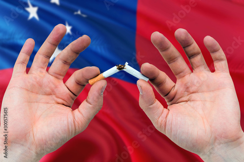Samoa quit smoking cigarettes concept. Adult man hands breaking cigarette. National health theme and country flag background.