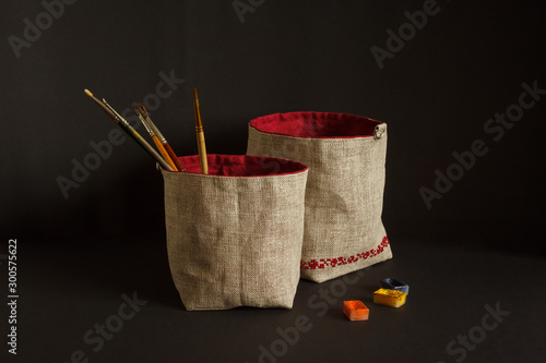 Bag for things with embroidery red ornament. Made of linen fabric. Paint brushes lie in a bag. Black background