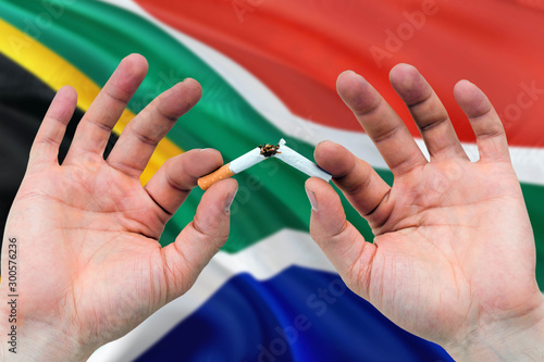 South Africa quit smoking cigarettes concept. Adult man hands breaking cigarette. National health theme and country flag background.