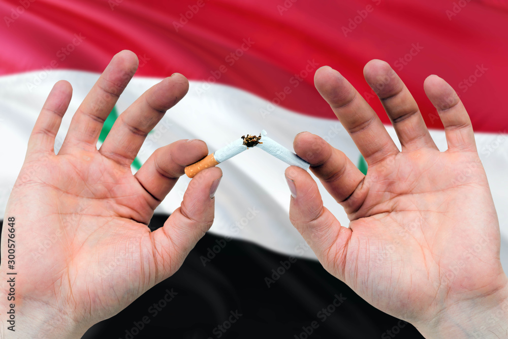 Syria quit smoking cigarettes concept. Adult man hands breaking cigarette. National health theme and country flag background. Syria quit smoking cigarettes concept. Adult man hands breaking cigarette. National health theme and country flag background.
