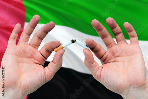 United Arab Emirates quit smoking cigarettes concept. Adult man hands breaking cigarette. National health theme and country flag background.