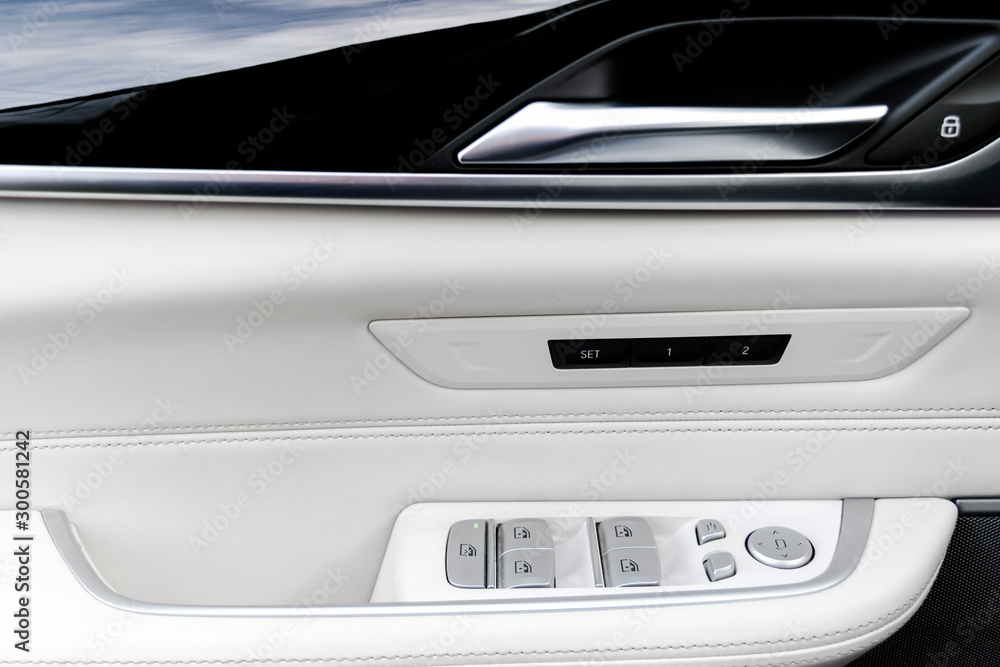 Door handle with power window control buttons of a luxury passenger car. White perforated leather interior with stitching and natural wood panel. Modern car interior details. Car detailing. Car inside