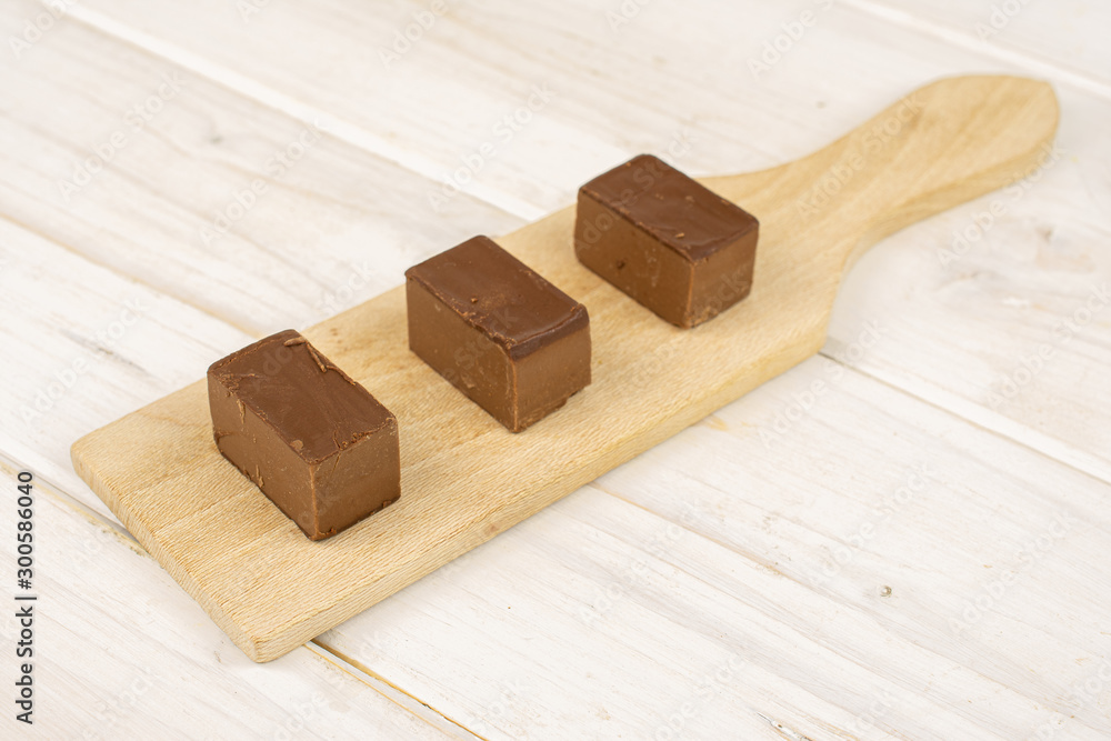 Group of three whole sweet brown viennese nougat on small wooden cutting board on white wood