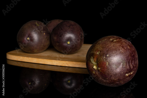 Group of four whole sweet dark purple passion fruit on bamboo cutting board isolated on black glass