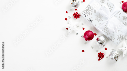 Top view Christmas present and silver and red decor elements on white background. Flat lay gift box with ribbon bow, balls, stars, confetti. Christmas, winter holiday, New Year concept.