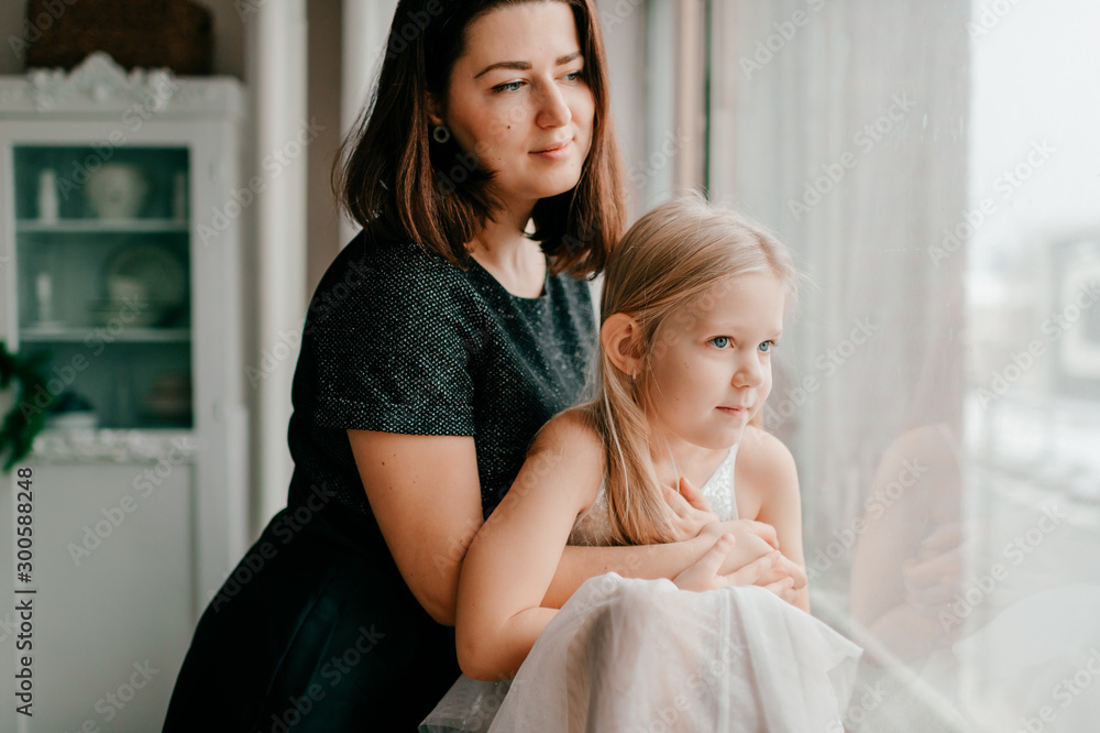 Young happy mother hugs her beautiful daughter looking at window Young happy mother hugs her beautiful daughter looking at window