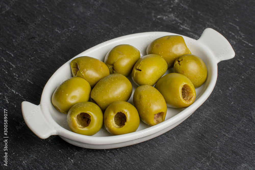 Lot of whole pitted green olive in white oval ceramic bowl on grey stone Lot of whole pitted green olive in white oval ceramic bowl on grey stone