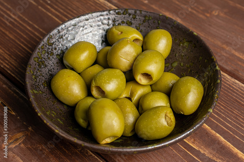 Lot of whole pitted green olive in dark ceramic bowl on brown wood