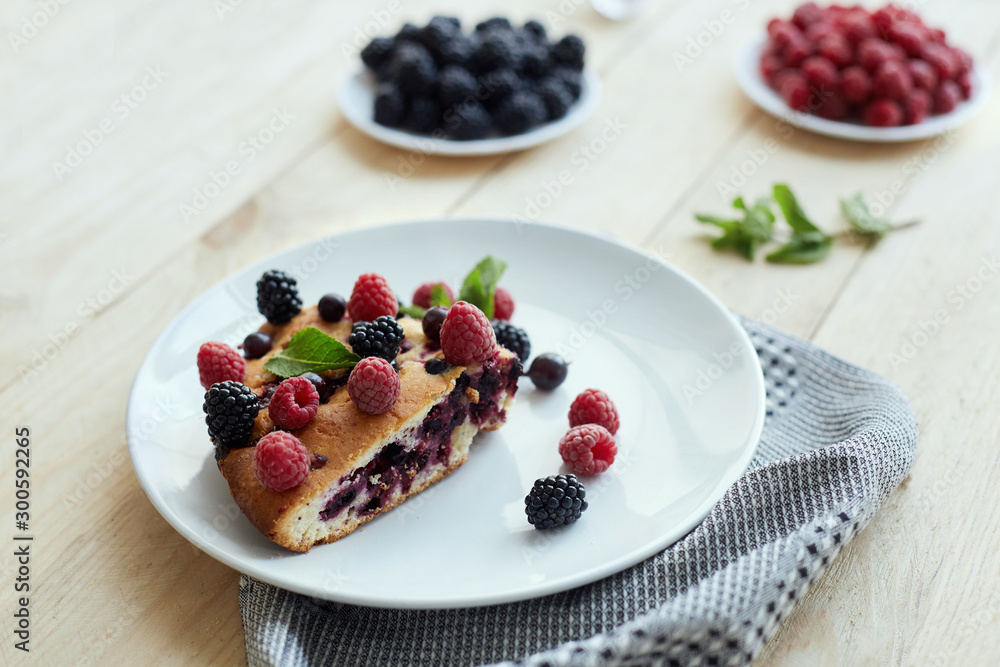 Piece of pie with blueberries, raspberry and mint for dessert on a white plate, napkin. Pieces of delicious homemade cake on a wooden boards background Piece of pie with blueberries, raspberry and mint for dessert on a white plate, napkin. Pieces of delicious homemade cake on a wooden boards background