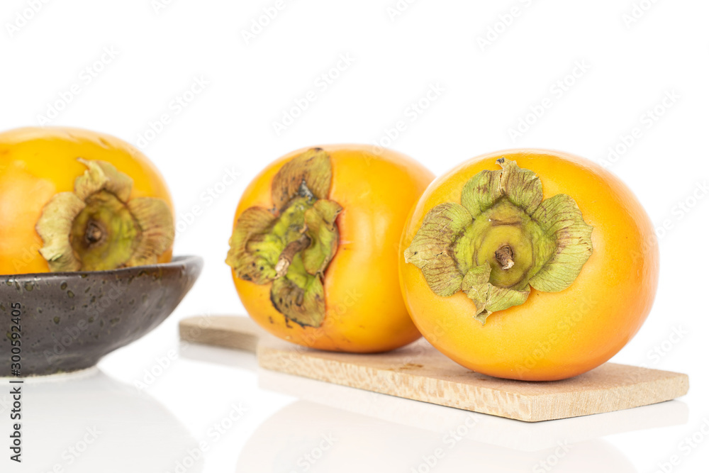Group of three whole sweet orange persimmon in glazed bowl on wooden cutting board isolated on white background