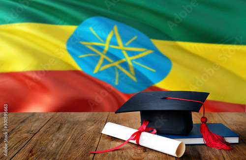 Ethiopia education concept. Graduation cap and diploma on wooden table, national flag background. Succesful student.