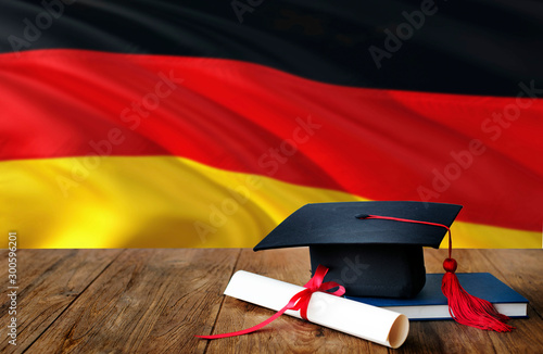 Germany education concept. Graduation cap and diploma on wooden table, national flag background. Succesful student.