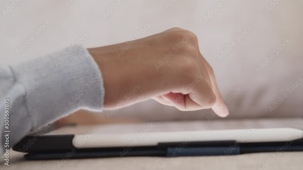 Hand of little girl touches the white digital tablet screen while placing the tablet on the sofa at home. Hand of little girl touches the white digital tablet screen while placing the tablet on the sofa at home.