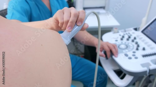 Doctor makes ultrasound of shoulder joint to man using ultrasound scanner in clinic, closeup. He runs ultrasound sensor over man's arm, working on scanner panel and looking at screen.