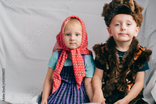 Beautiful couple of lovely children in bear costume and russian cartoon clothes sitting on bed with funny faces. Soft focus portrait of little children in costumes