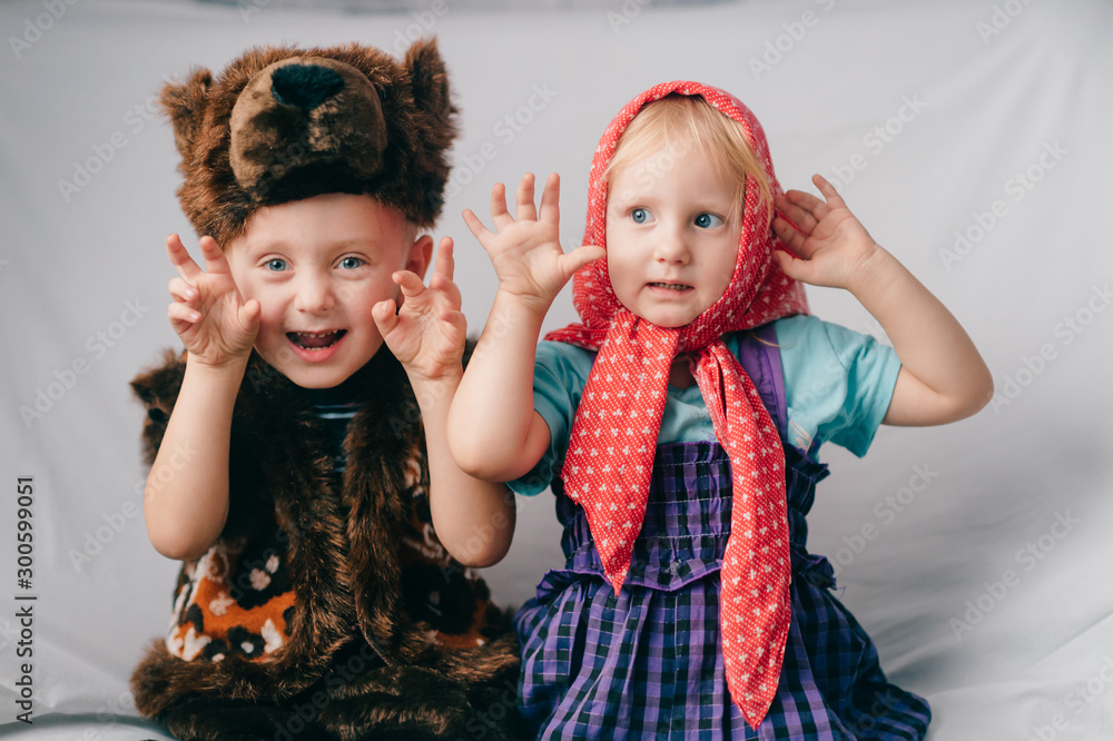 Beautiful couple of lovely children in bear costume and russian cartoon clothes sitting on bed with funny faces. Soft focus portrait of little children in costumes Beautiful couple of lovely children in bear costume and russian cartoon clothes sitting on bed with funny faces. Soft focus portrait of little children in costumes