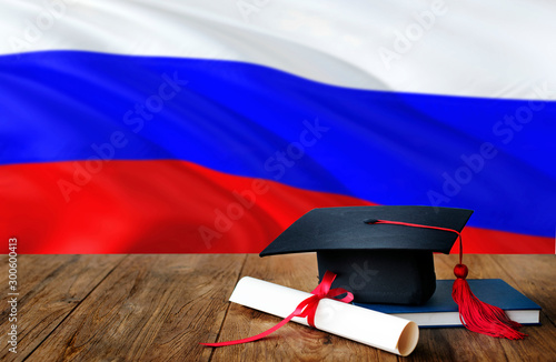 Russia education concept. Graduation cap and diploma on wooden table, national flag background. Succesful student.