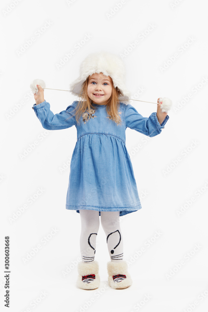 Smiling little surprised girl in a blue dress and a winter white fur hat having fun on White isolated background Smiling little surprised girl in a blue dress and a winter white fur hat having fun on White isolated background