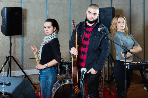 Three bandmates posing together with musical instruments in rehearsal room
