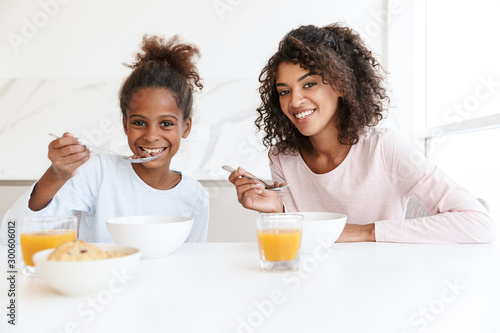 Image of american woman and her daughter having breakfast in kitchen