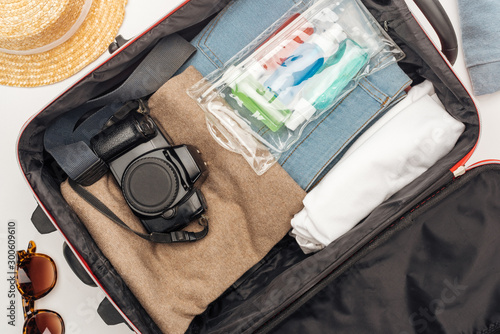 top view of travel bag with towel, cosmetic bag with colorful bottles, digital camera, clothes