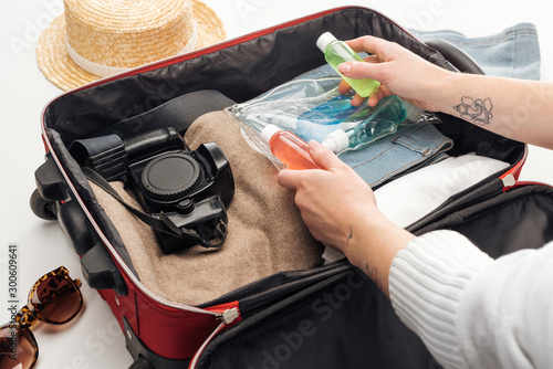 cropped view of woman packing travel bag with cosmetic bag with colorful bottles