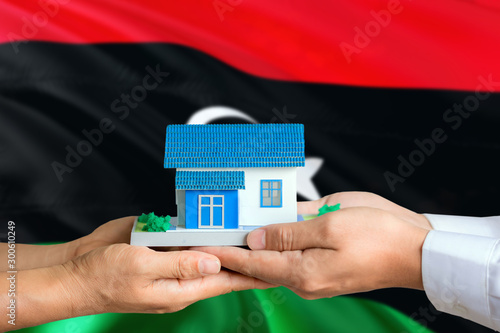 Libya real estate concept. Man and woman holding miniature house in hands. Citizenship theme and national flag on background.