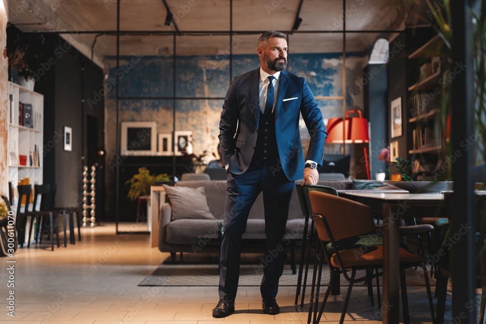 Stylish bearded man in a suit standing in modern office Stylish bearded man in a suit standing in modern office
